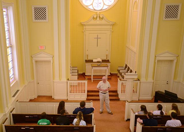 {Male professor addresses a small group of students int he college chapel}